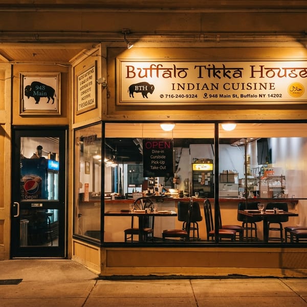 Exterior of Buffalo Tikka House at night, with illuminated signs and a view into the dining area.