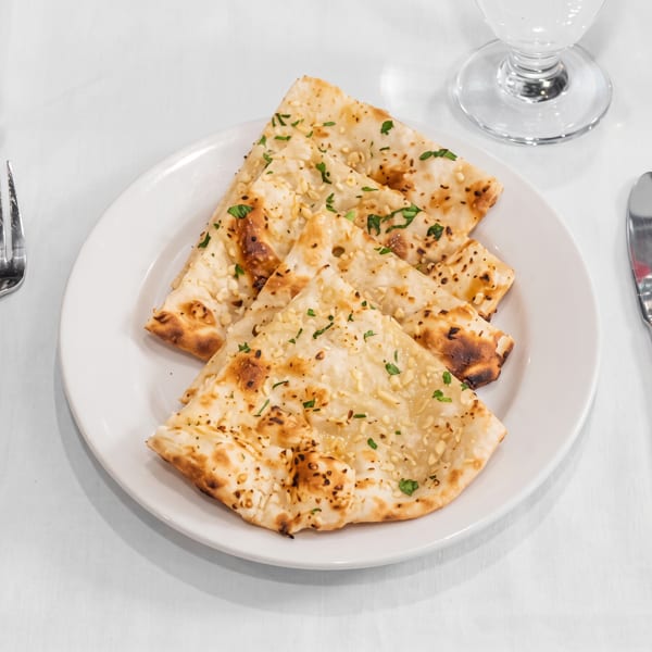 White plate with triangular pieces of naan bread topped with sesame seeds and herbs on a white tablecloth.