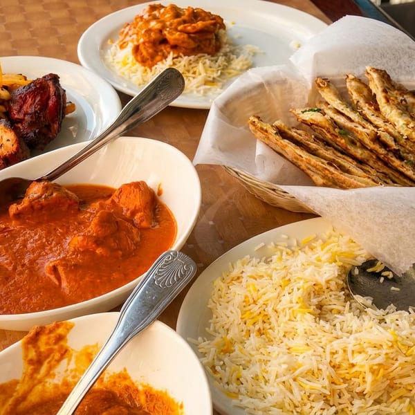 A table laden with various Indian dishes including chicken tikka, butter chicken, rice, and naan bread.